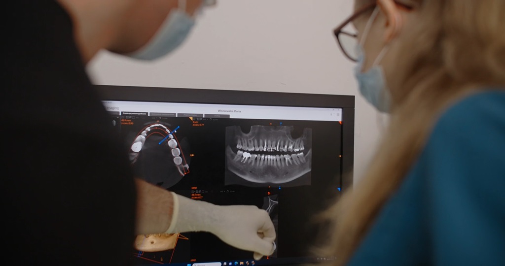 Two orthodontists wearing masks analyzing 3D dental scans and X-ray images on a computer screen in a clinical setting.