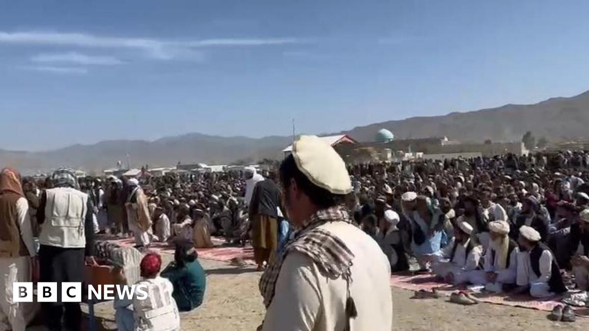 A large crowd of likely hundreds of people seen outside beside mountains
