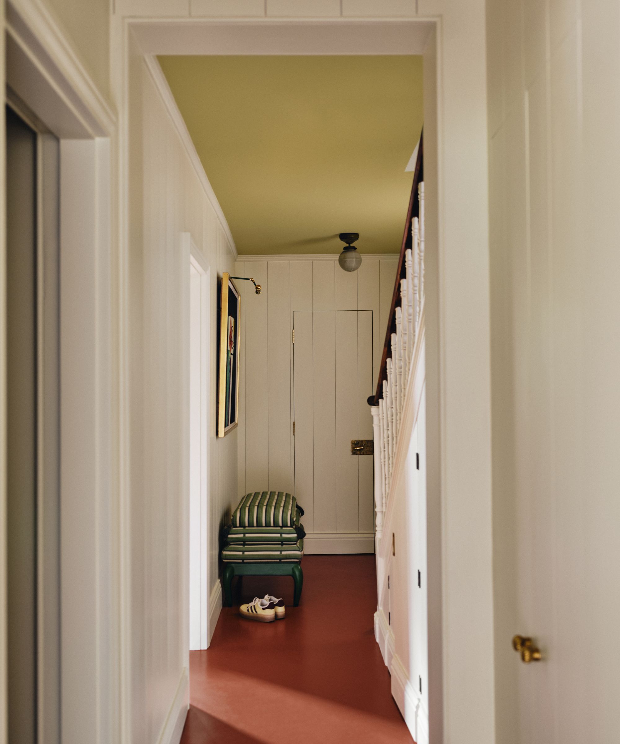 a small corridor hallway with a red painted floor and a butter yellow painted ceiling with white panelled walls