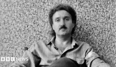 Henry Orlik sits in front of a painting with lots of squiggles - black & white photo