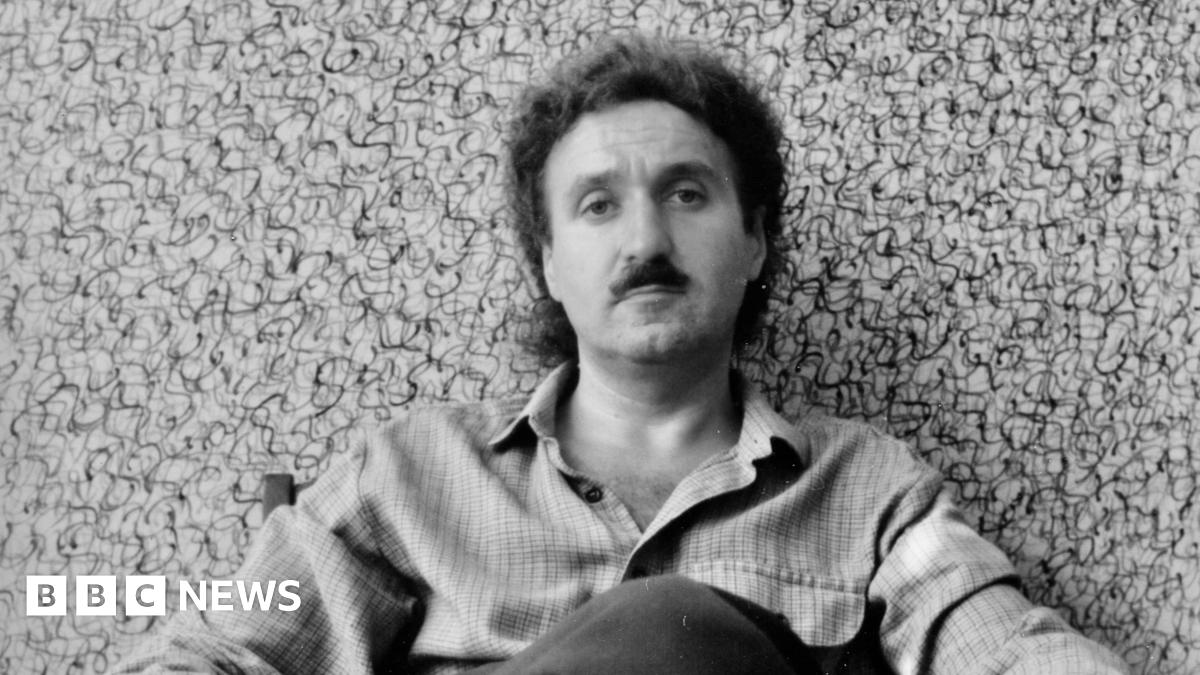 Henry Orlik sits in front of a painting with lots of squiggles - black & white photo