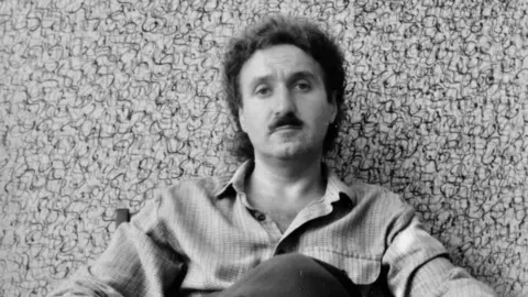 Henry Orlik Henry Orlik sits in front of a painting with lots of squiggles - black & white photo