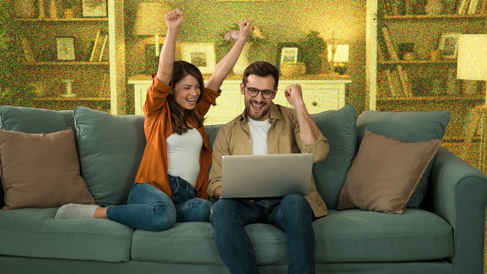 Young couple looking excited whilst sitting on sofa with a laptop.