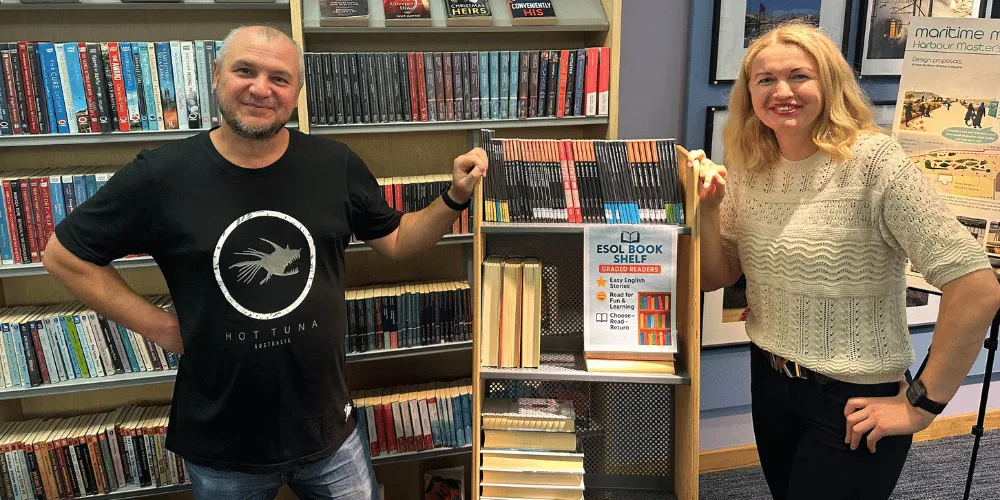 A man and a woman standing next to book shelves.