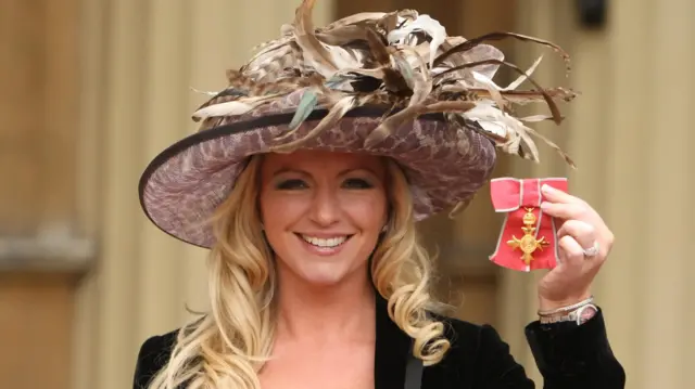Michelle Mone holding up her OBE medal outside Buckingham Palace