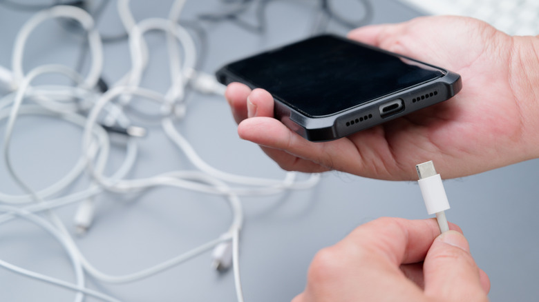 A person charging their phone, blurry background with a mess of cables
