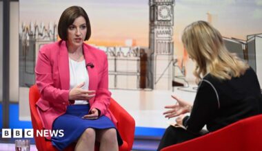 A large crowd of protesters holding Palestinian flags and placards are gathered with the Houses of Parliament in the background.