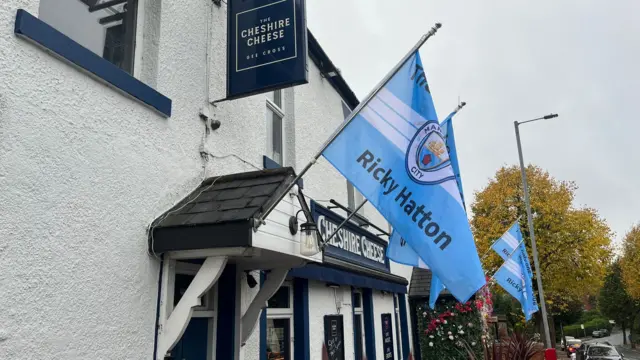 Manchester City flags with the name Ricky Hatton are flying outside a pub