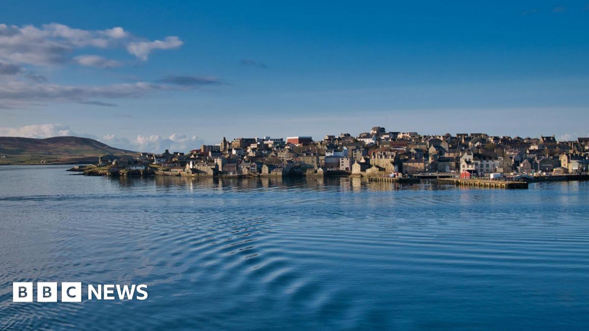 Houses and other buildings on the waterfront at Lerwick. There are ripples on the surface of the sea and the sky is blue.
