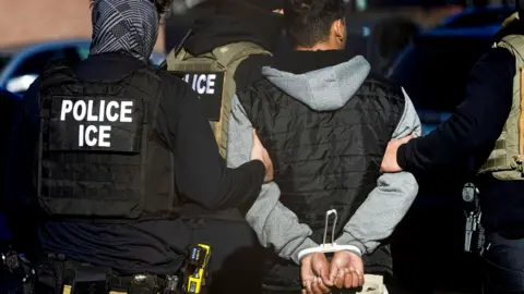 Reuters Image of three ICE agents with a man who has been detained and has his hands bound behind his back. 