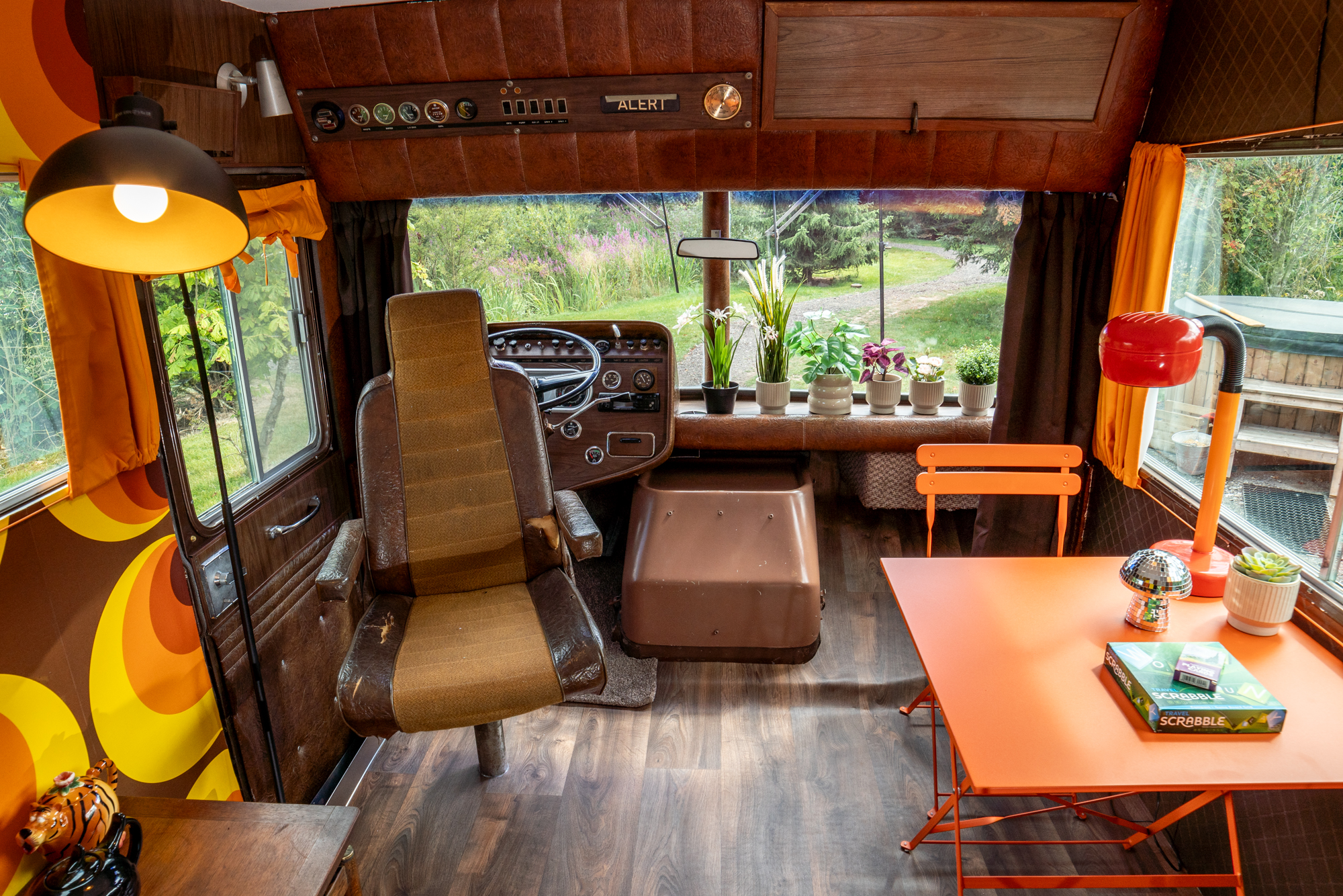 Interior of a converted vehicle glamping site, with a brown driver's seat, orange table, and potted plants.