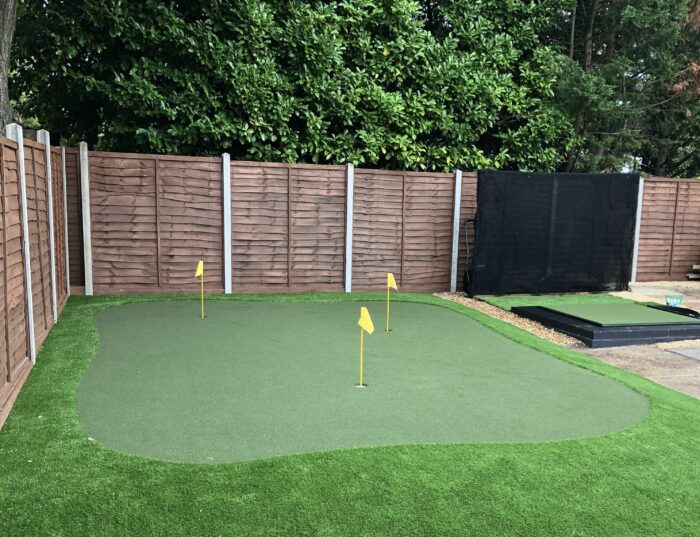 An all-weather green golf putting area with three yellow flags, surrounded by artificial grass.