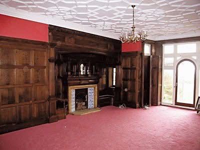 Before shot of a room with dark wood paneling, red walls, and a pink carpet.
