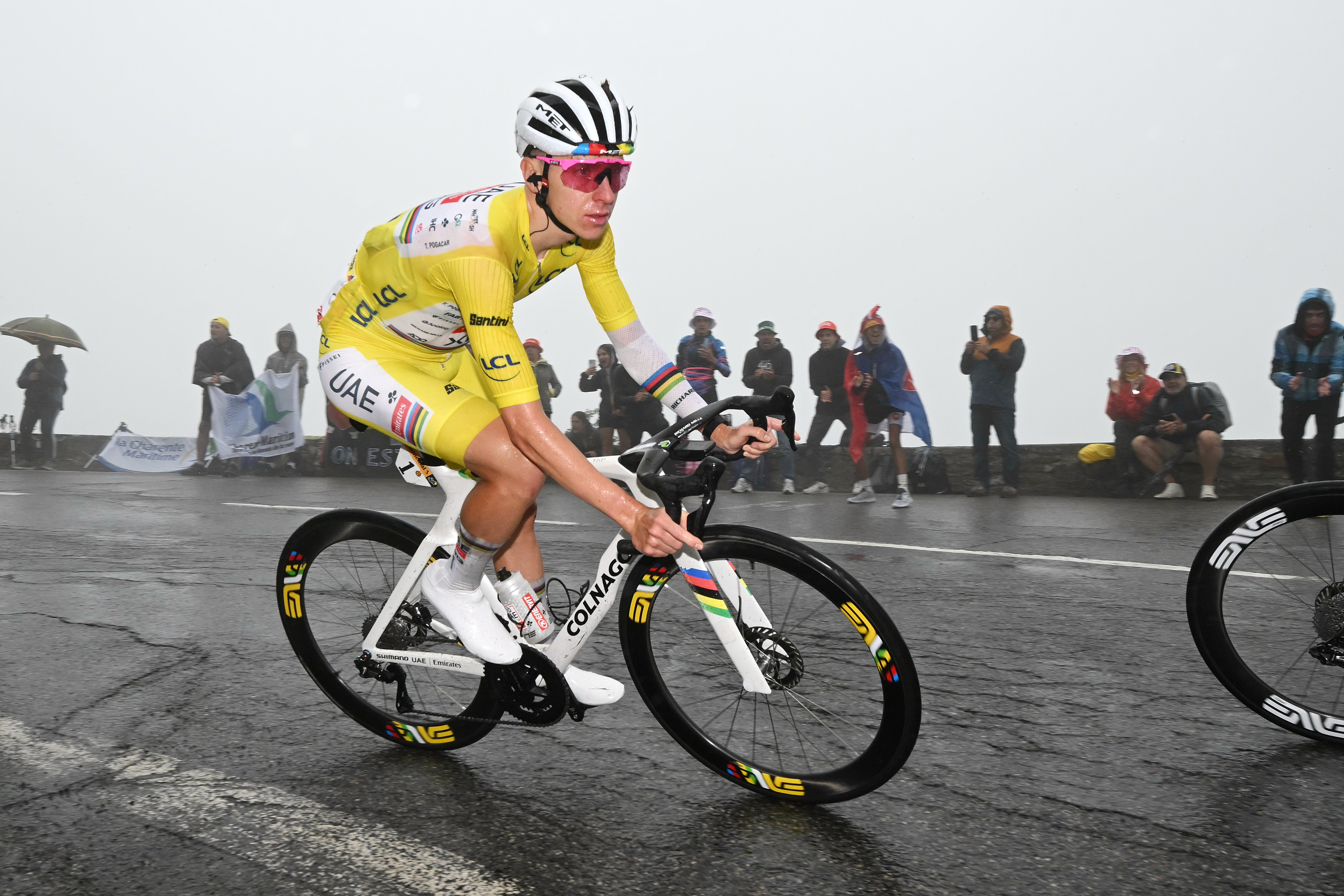 Tadej Pogacar in a yellow leader jersey cycling in the rain during the Tour de France.