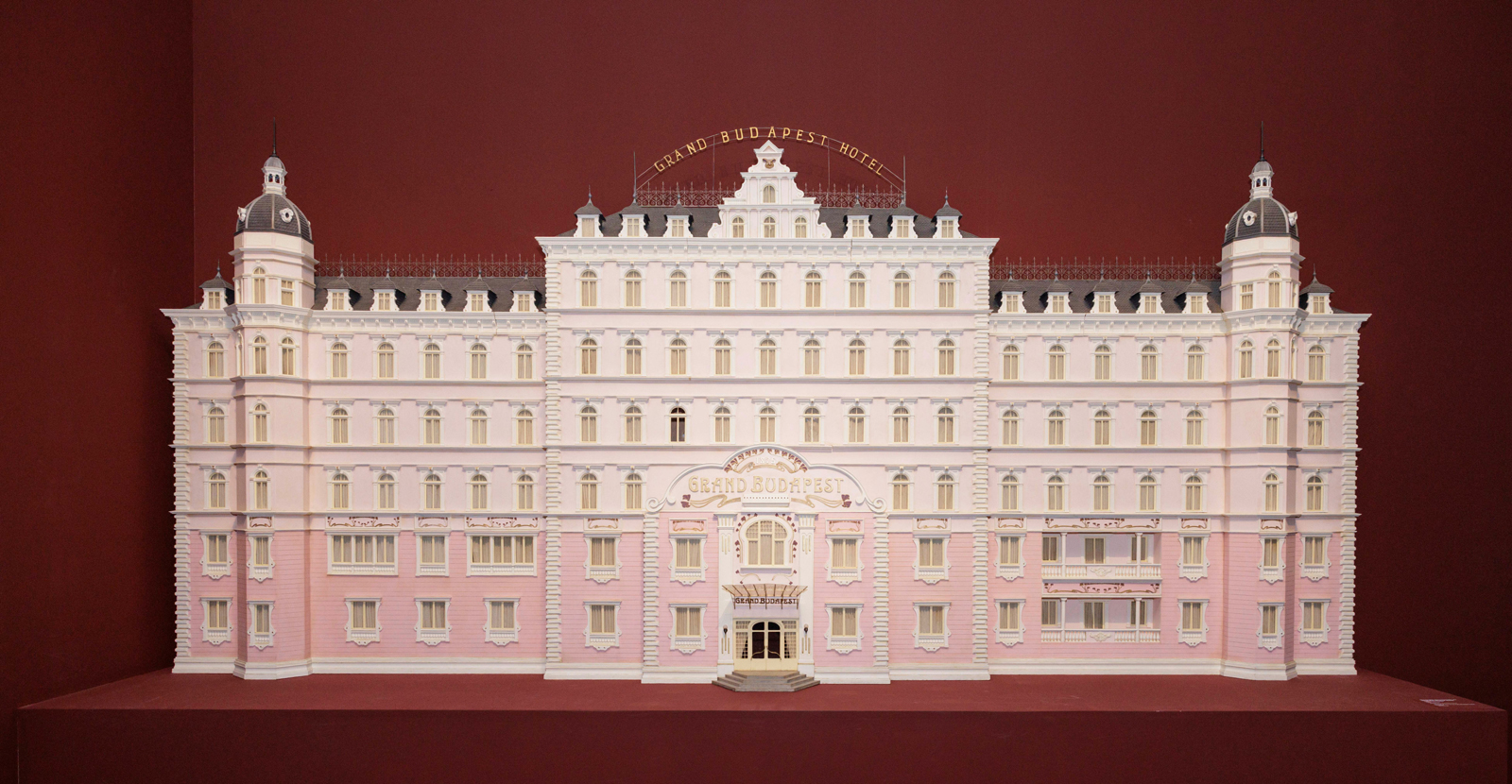 Model of the Grand Budapest Hotel, a large pink building with white trim, a gold sign, and two domed towers.