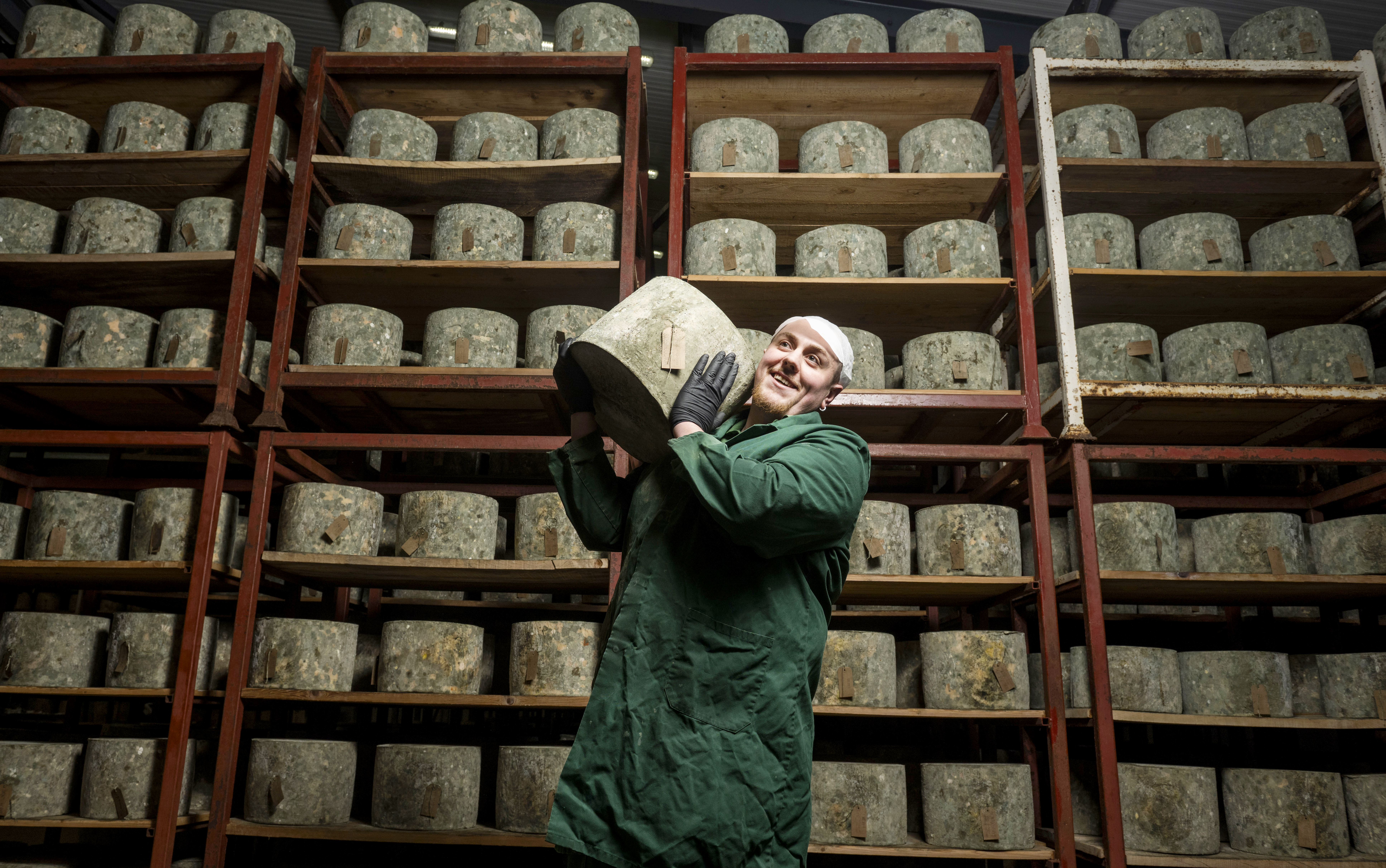 Duncan Bridges, a cheesemaker at Montgomery's Cheddar, inspecting cheddar wheels on shelves.
