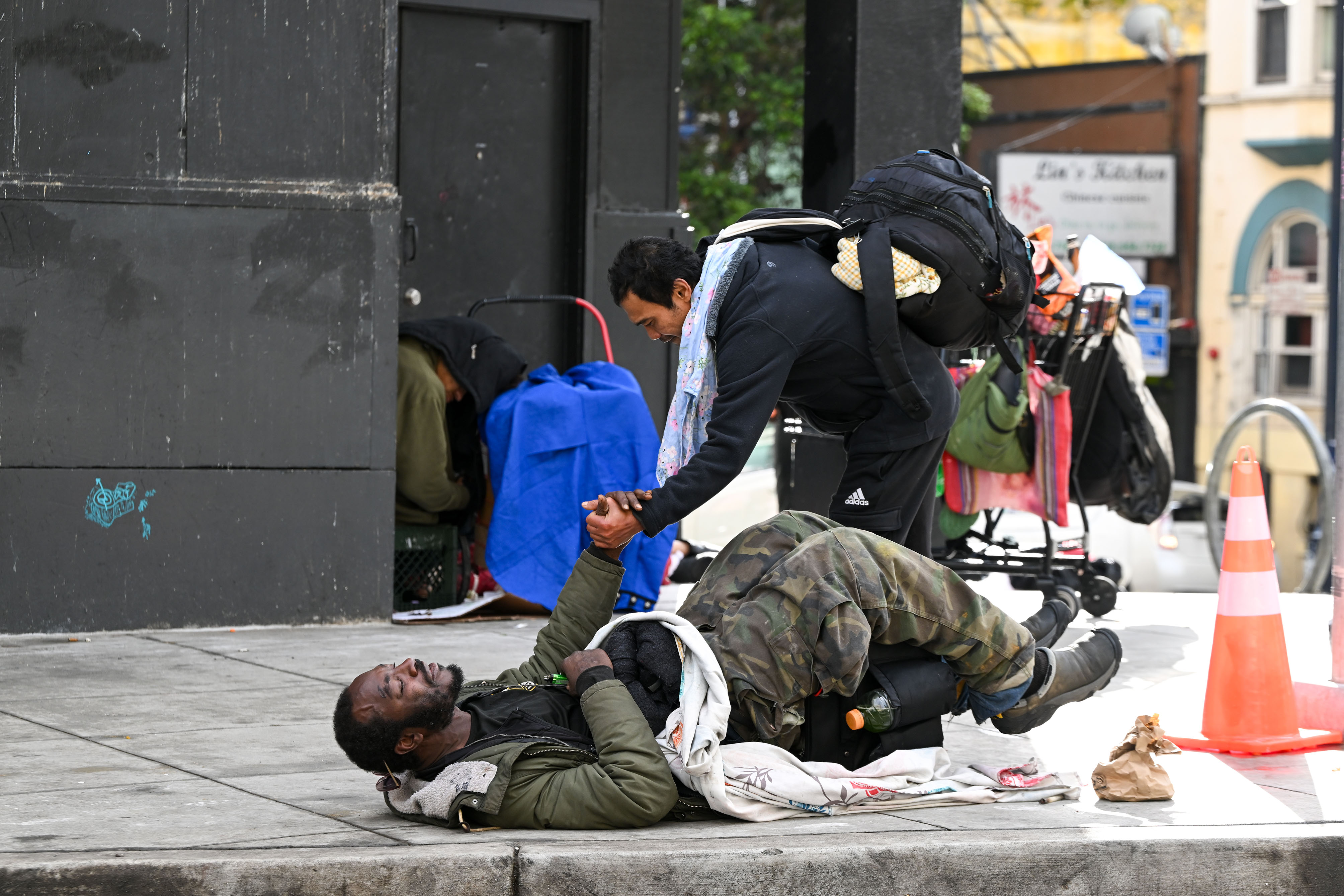 A man on the street helps another man who is lying on the ground.