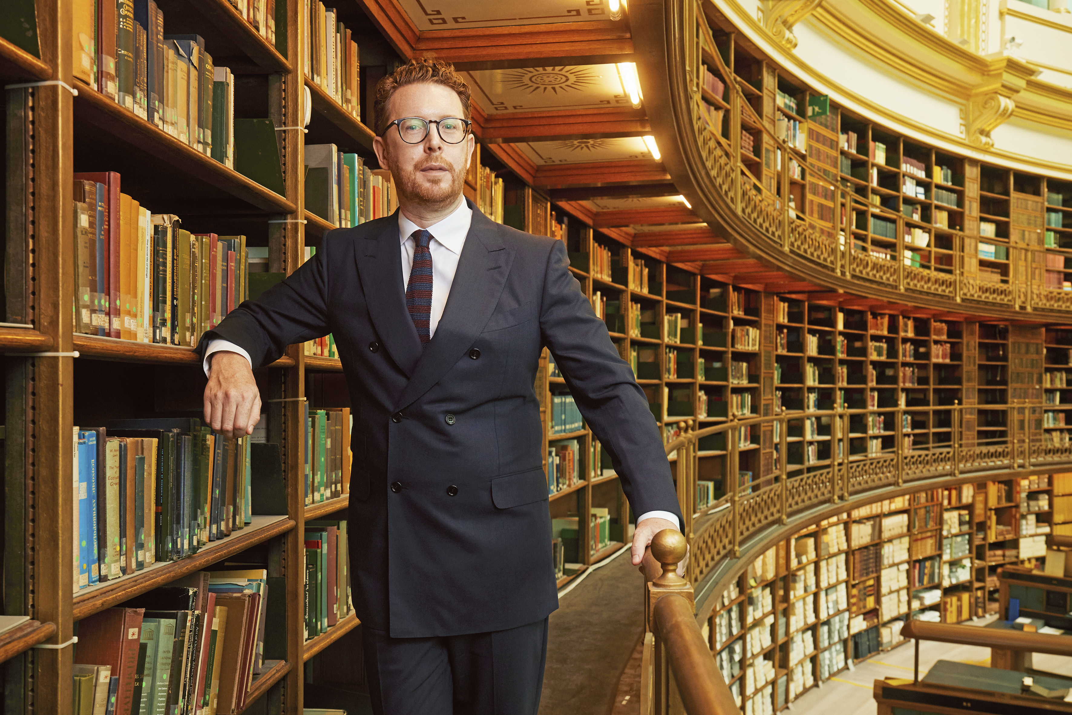 Dr. Nicholas Cullinan, Director of The British Museum, standing in a large, multi-story library.