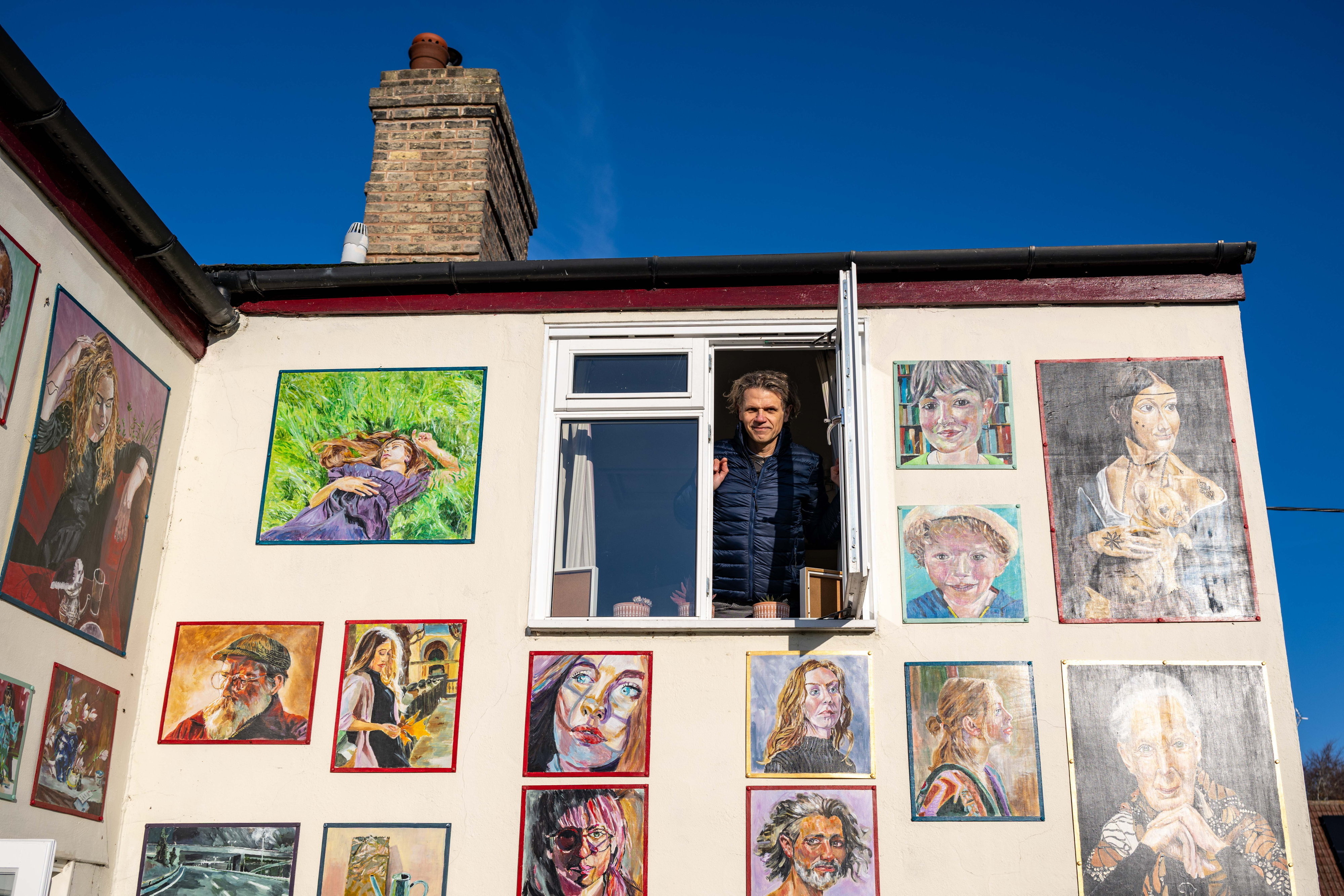 Robert Petryszak looking out from a window of his cottage, which is covered with his paintings of people, animals, and flowers.