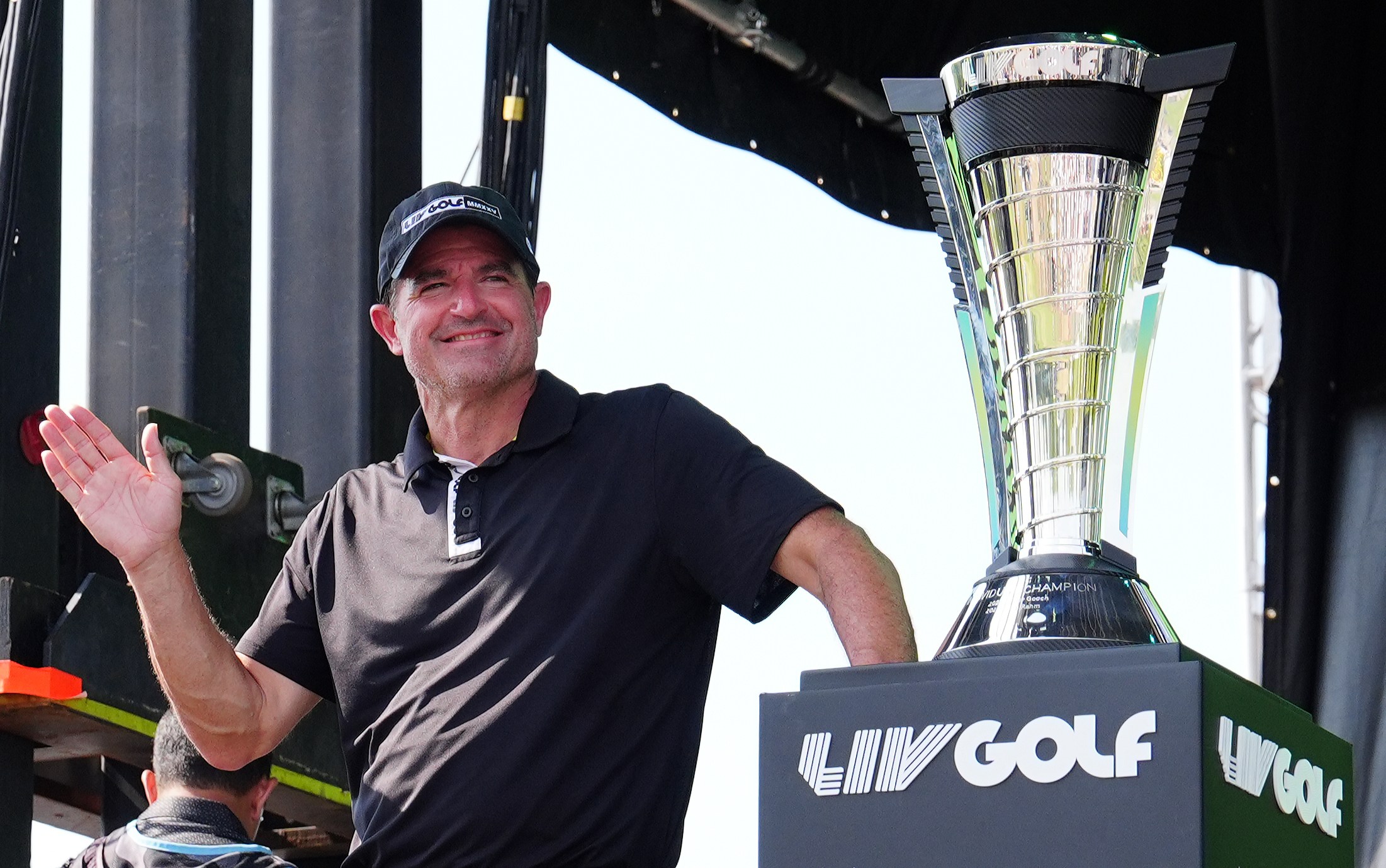 LIV Golf CEO Scott O'Neil waves next to the 2025 LIV Golf Championship trophy.