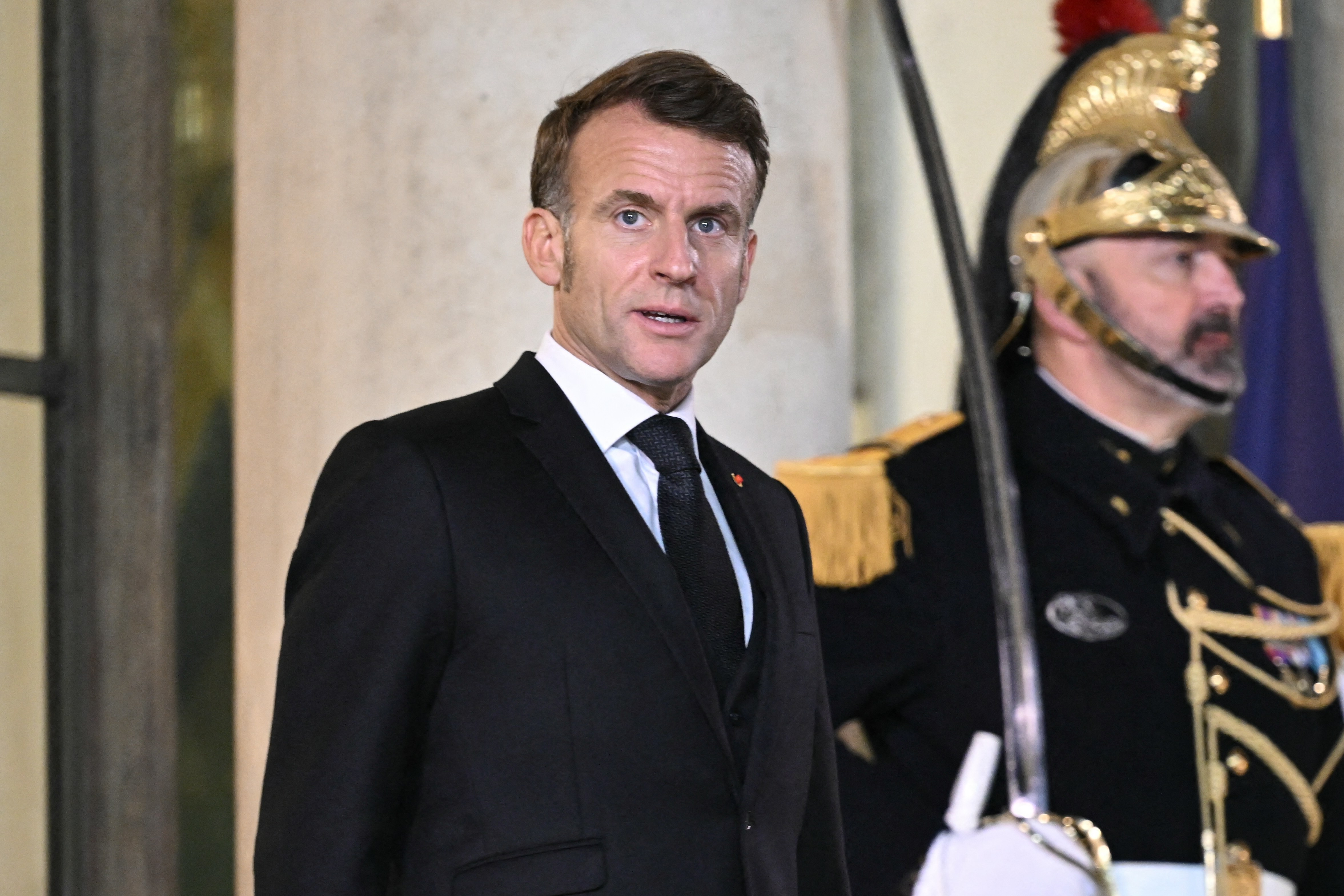 French President Emmanuel Macron and a guard in uniform stand at the Elysee Presidential Palace.