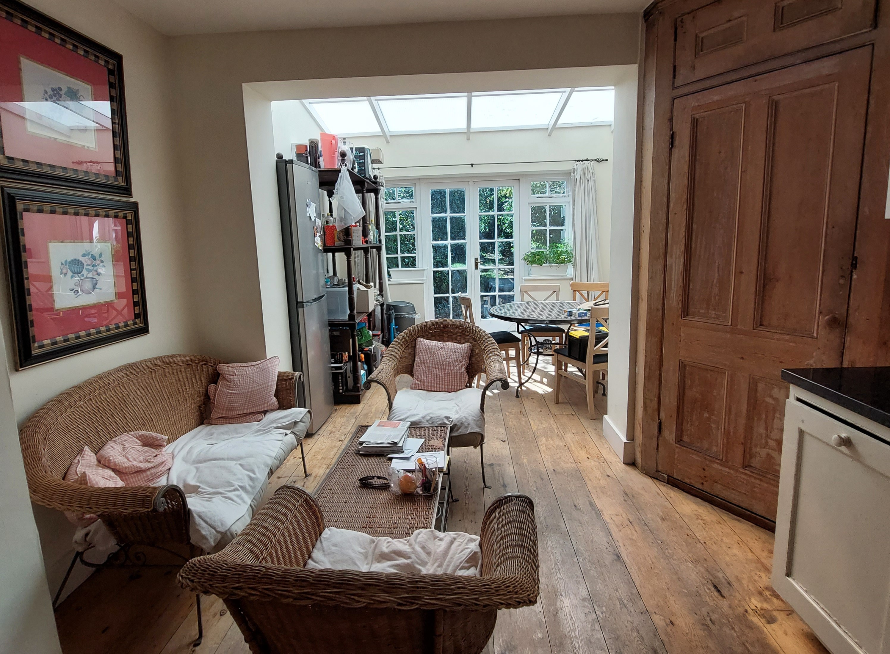 A long, narrow room with wooden floors and several wicker chairs, leading to a sunroom with French doors.