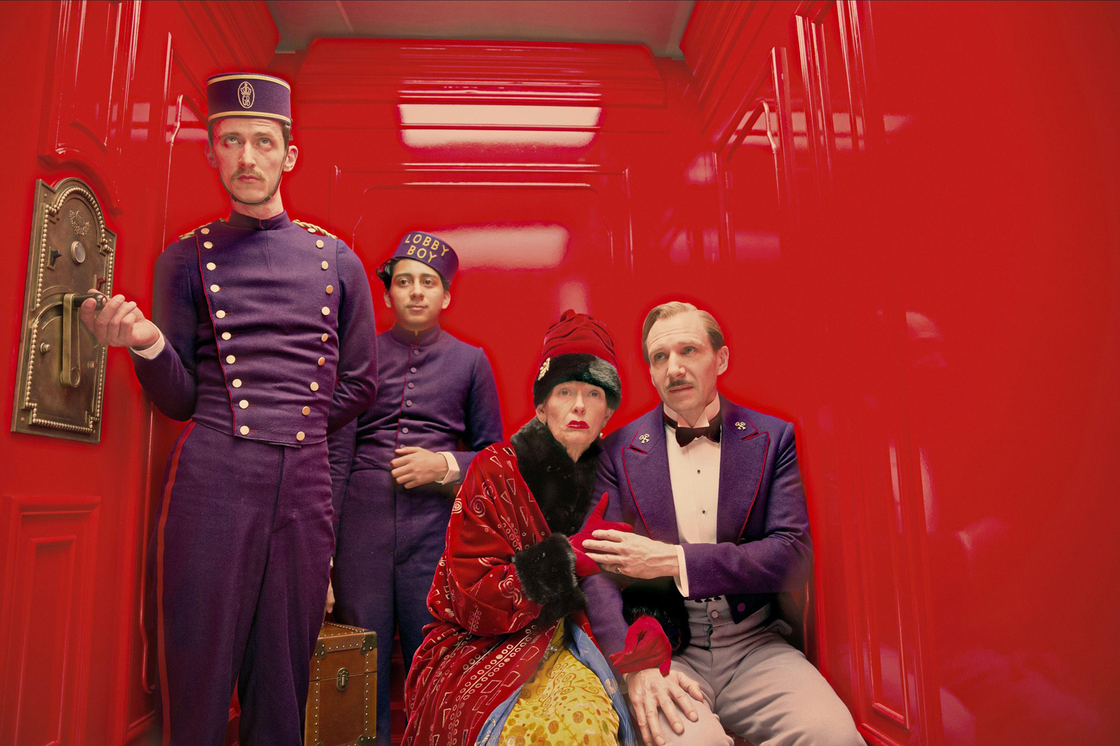 Four characters in a hotel elevator, wearing uniforms and elegant attire.