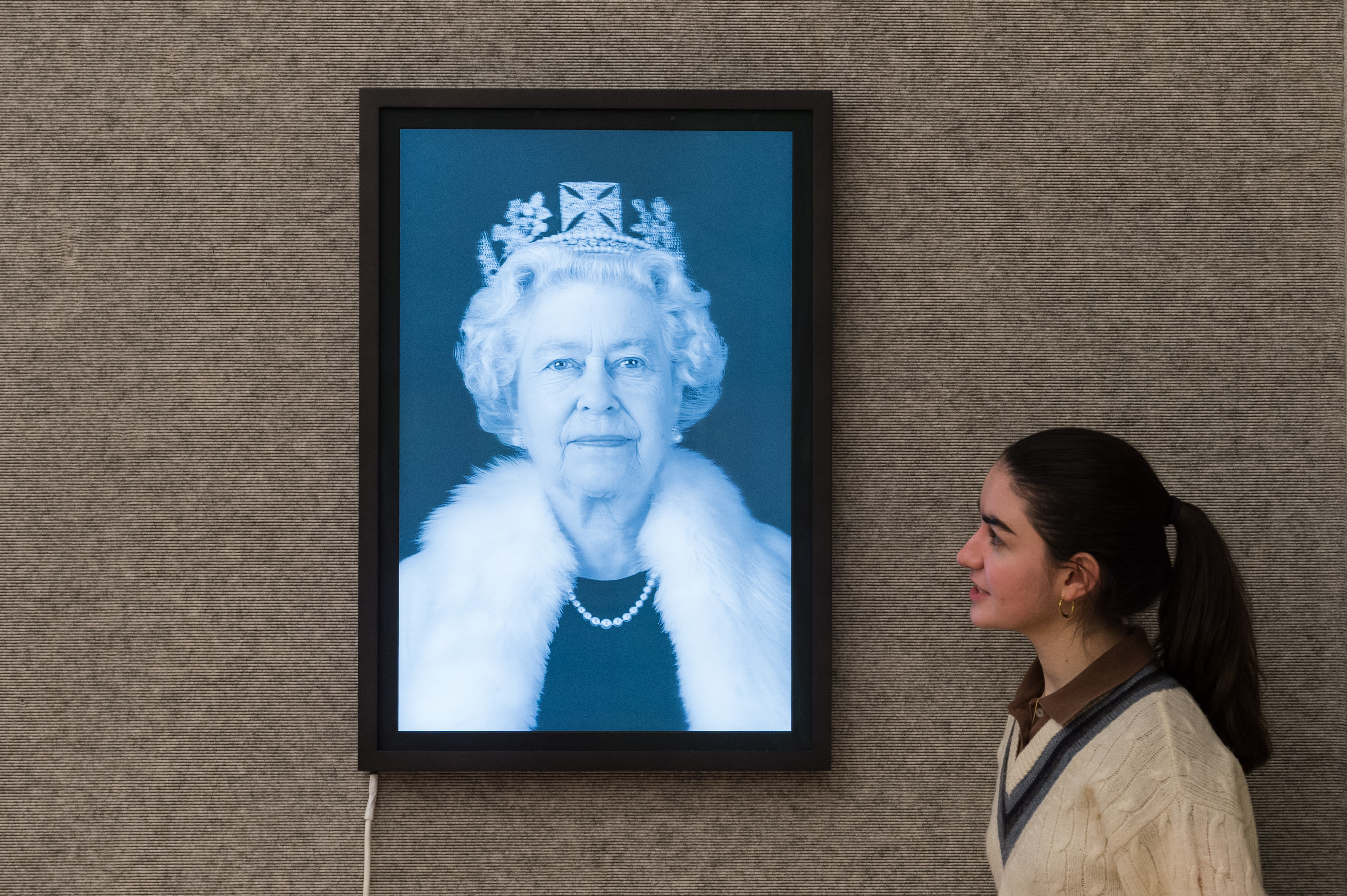 A staff member views a Chris Levine 3D lenticular print of Queen Elizabeth II in a lightbox.