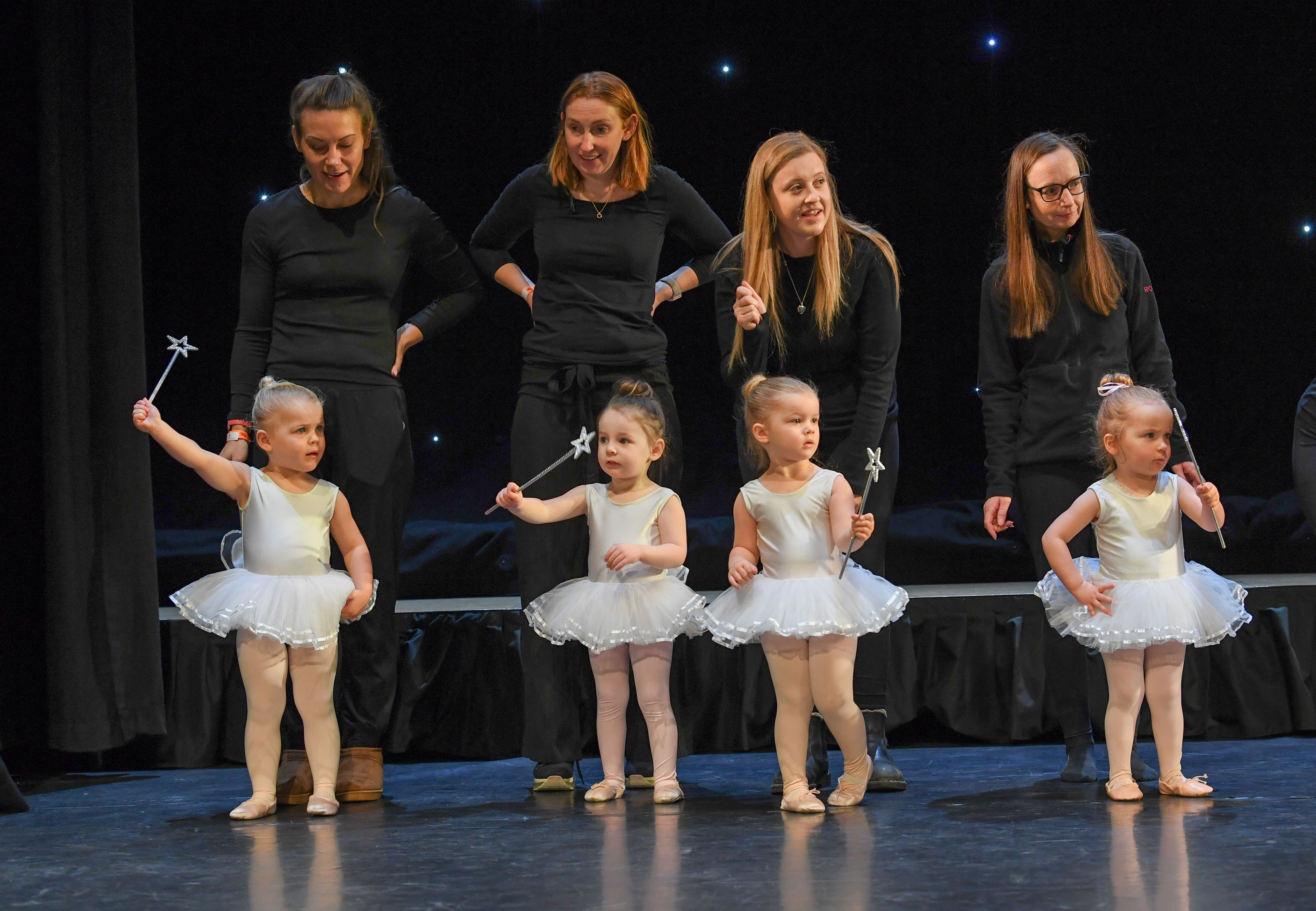Young ballet dancers with teachers on stage during a performance.