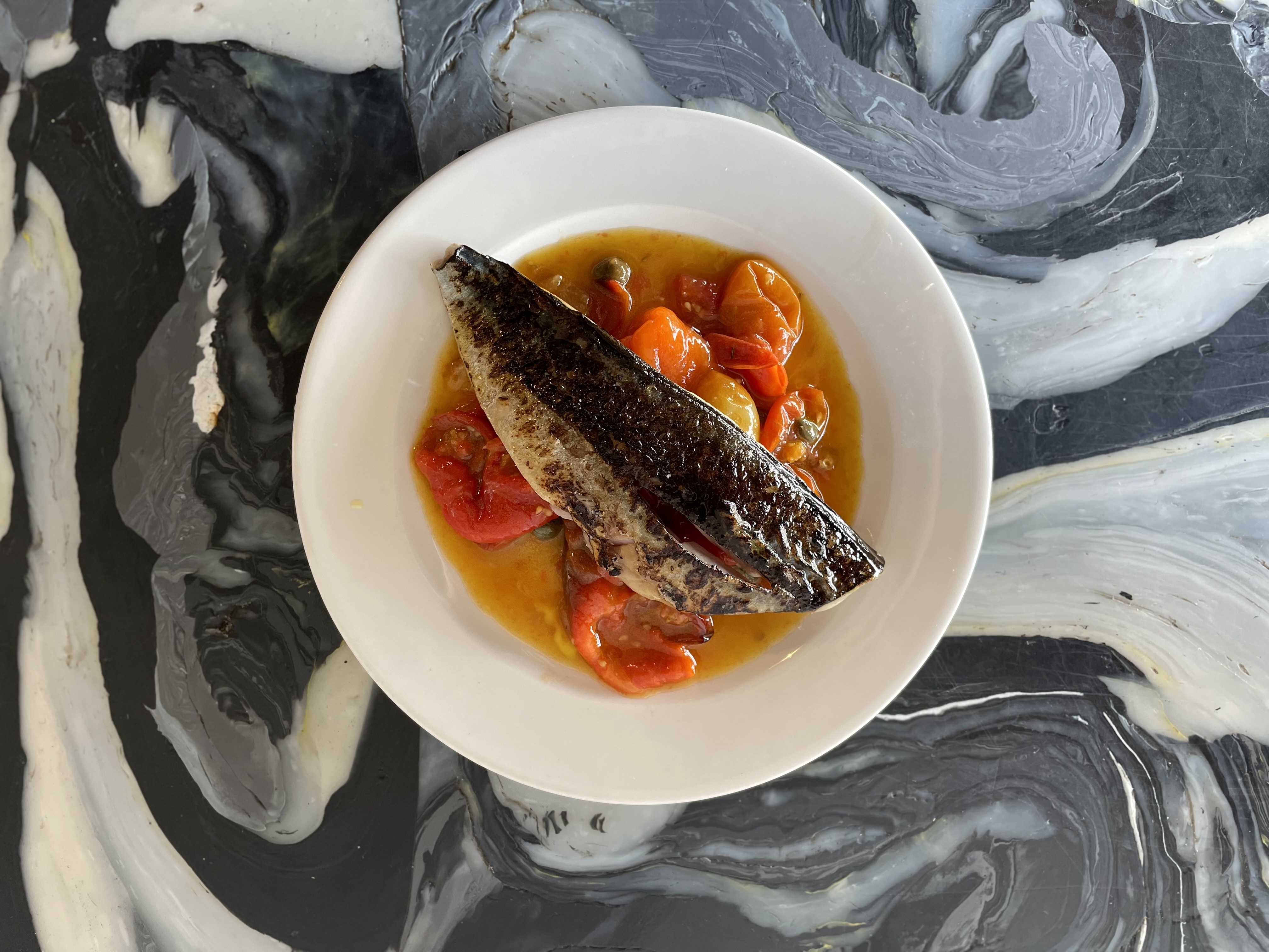 Grilled fish with roasted tomatoes on a white plate.