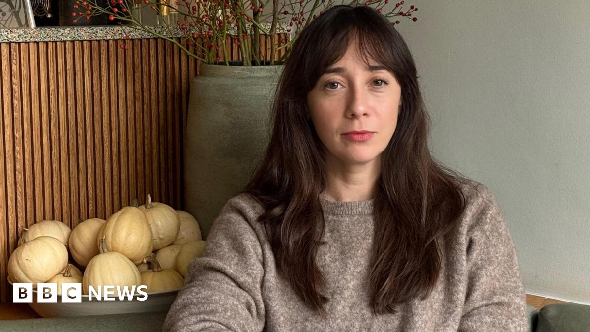 A woman with long dark brown hair looks sadly at the camera