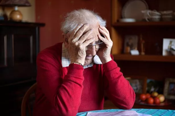 Senior male with his head in hands sitting at a table looking at bills