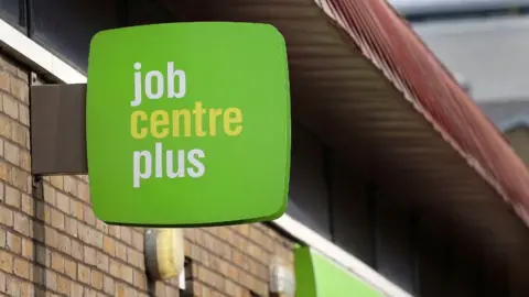 PA Media A green job centre plus sign on a brick outdoor wall 