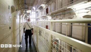 A man in uniform walks down a landing of prison cells.