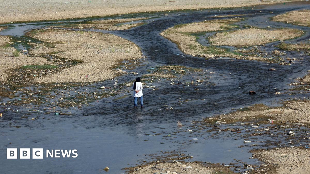 A woman stands by an almost entirely dried out river in Tehran that was once full