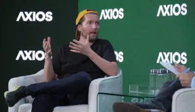 A man in a baseball hat talks and gesticulates on stage
