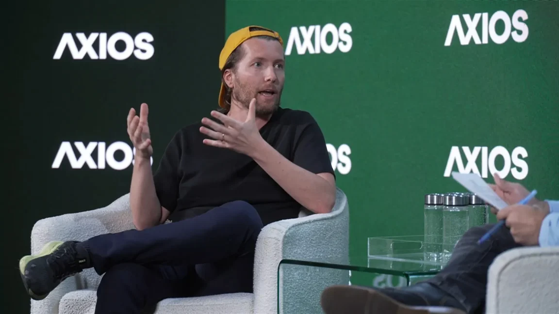 A man in a baseball hat talks and gesticulates on stage