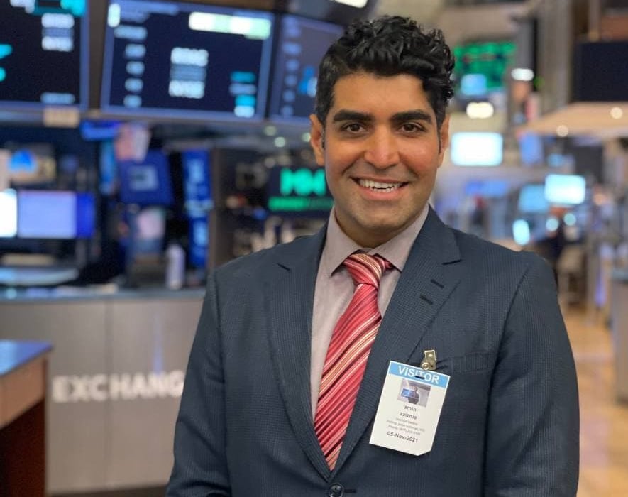 Man with dark in dark suit and bright tie stands smiling on the floor of the New York stock exchange