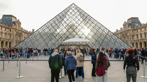 Getty Images A queue of hundreds of people are lined up outside the Louvre's iconic pyramid-shaped glass entrance
