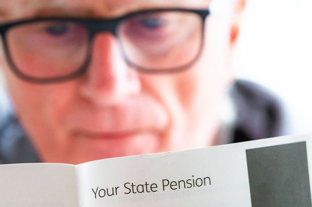 A retired senior man in his 70s reads information about receiving his pension. Focus on the leaflet with the man slightly defocused in the background.