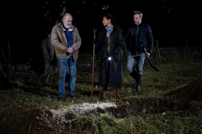 Bear, Celia and Ray stand beside a freshly dug grave in Emmerdale