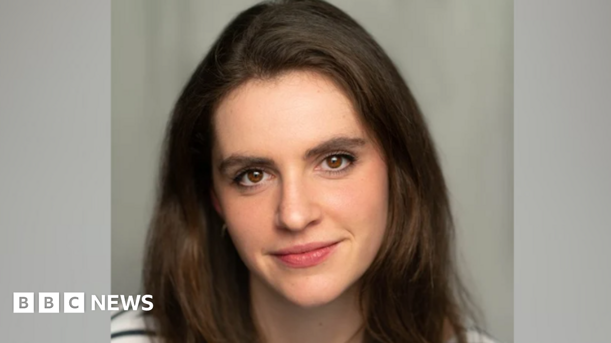 A close-up picture of Clementine Collett. She has long brown hair and brown eyes and is wearing a black and white striped T-shirt. Behind her is a grey background.
