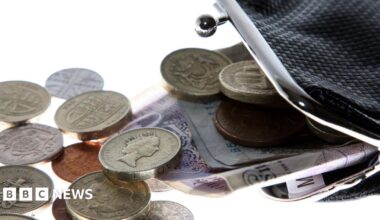 A black purse with the clasp open and money spilling out.