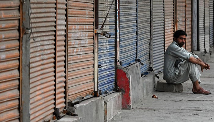A man sits idly in front of closed shops along a roadside in Peshawar on September 2, 2023, during a nationwide strike by traders. — AFP