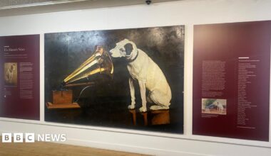 A painting of a white dog with black ears listening into a Gramophone.