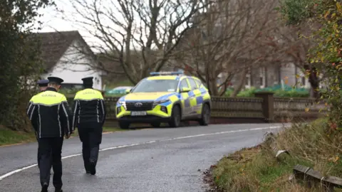 PA Media A Garda patrol car is parked at a road junction with two Garda officers standing nearby.