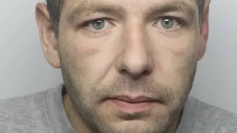 Dyfed-Powys Police Mugshot of a man with a short beard, wearing a grey jumper. 