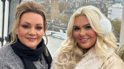 Breege Gormley Breege Gormley has dark blonde hair and is wearing a black scarf and grey overcoat. She is pictured with her daughter Jenny on the London Eye. 
Jenny has bright blonde hair and is wearing white earmuffs and a white jacket. 
