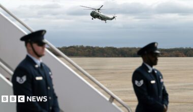 Marine Two lands at Joint Base Andrews, while two uniformed officers guard the steps to a plane on the tarmac.