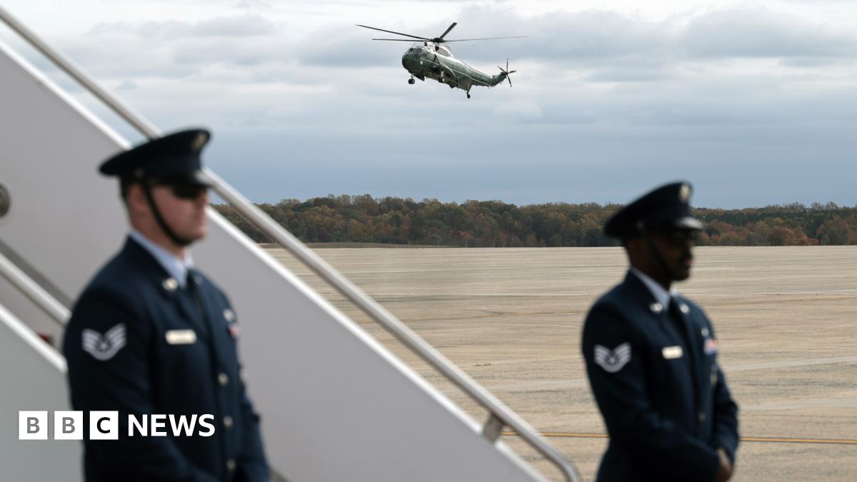 Marine Two lands at Joint Base Andrews, while two uniformed officers guard the steps to a plane on the tarmac.